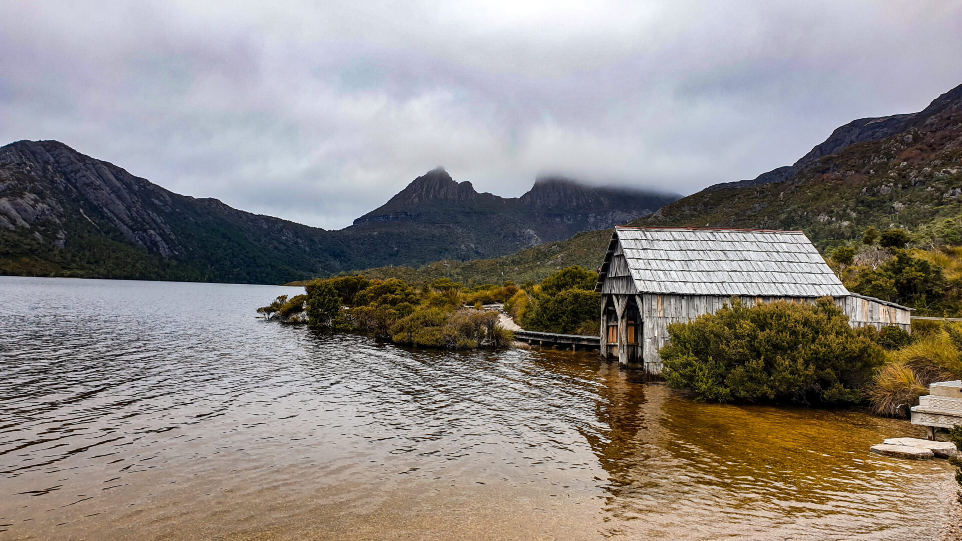 A boat shed on a lake with cloudy views of Cradle Mountain